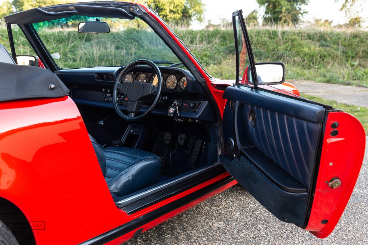 Puerta abierta del Porsche 911 SC Cabriolet 1983 mostrando el interior en cuero azul